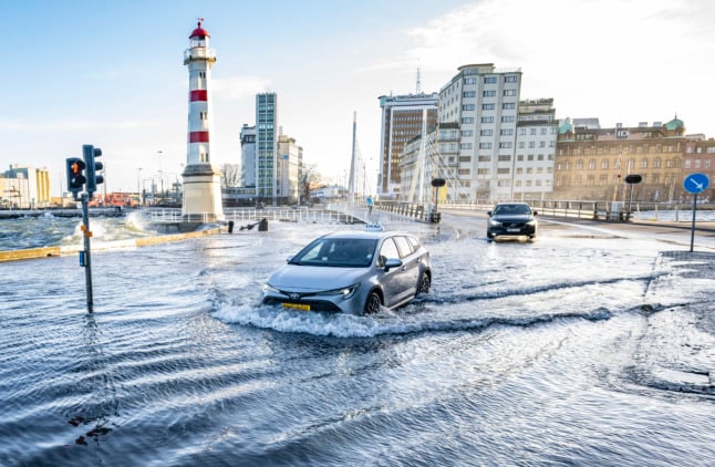 Cars wade through the water on the road by the lighthouse in Sweden's Malmö Harbour