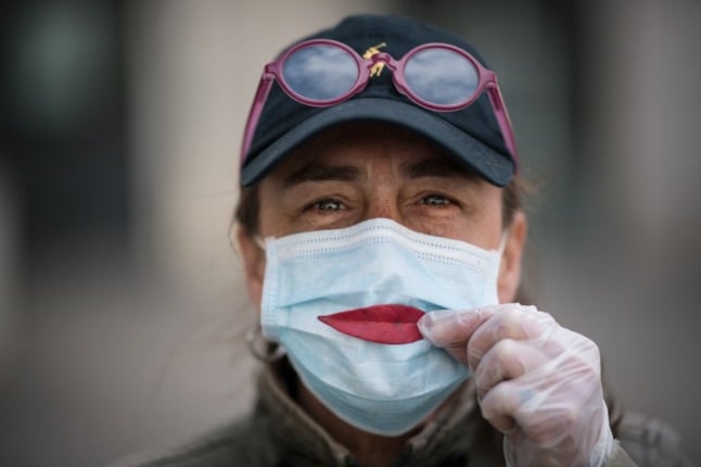 A woman in France holds a leaf to her face mask to make a smile.