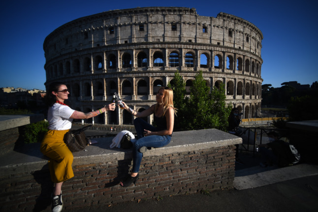 Young women clink bottles of beer as they share an aperitif drink by the Colosseum monument in Rome on May 21, 2020,