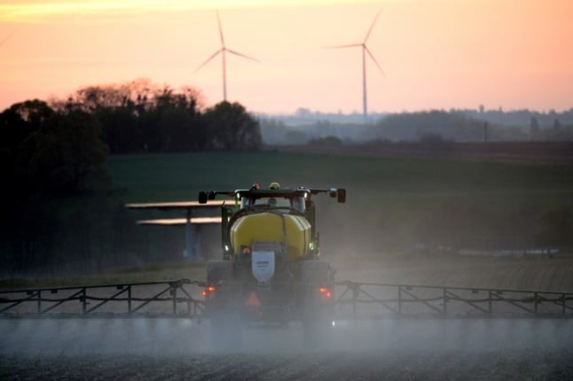 A French farmer sprays herbicide as wind turbines mark the skyline.