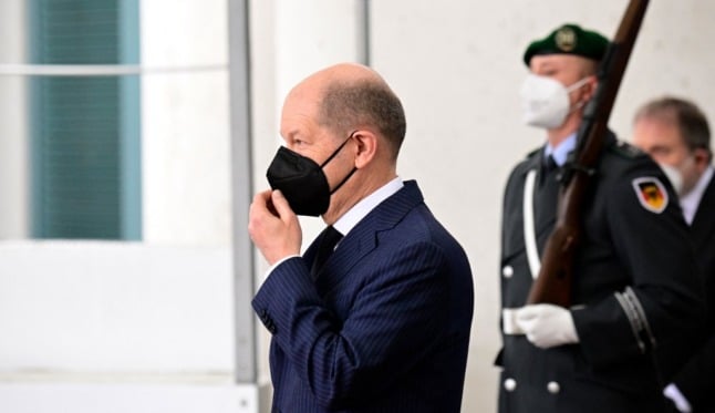 Olaf Scholz in a face mask in front of armed guards