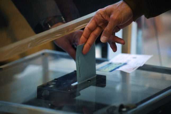 The hands of a voter and an election official over the ballot box as a vote is cast at a polling station in France