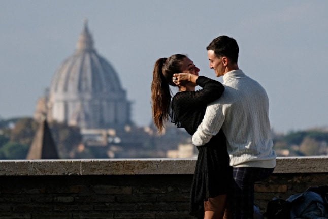 A young couple embraces on a terrace of the Oranges Gardens (Giardino degli Aranci) on Aventine Hill overlooking The Vatican's St. Peter's Basilica (Rear) in Rome on November 11, 2020, during the government's restriction measures to curb the spread of COVID-19 novel coronavirus. - Italy has shut bars, restaurants and shops in the worst-affected areas and introduced a nationwide night curfew, but has so far swerved a second shutdown, with the antigen tests becoming a crucial part of its efforts.