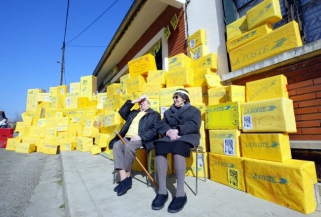 Two pensioners sit by a wall of packages. 