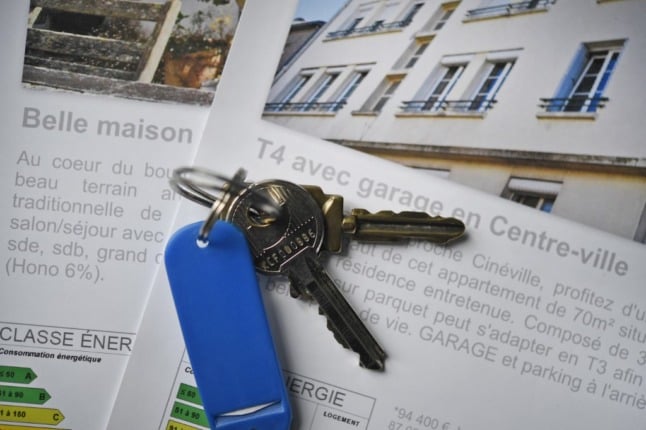 A set of house keys on a blue plastic fob on top of property adverts at an estate agents in northwest France