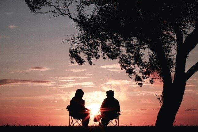 A couple sitting on chairs beneath a tree, silhouetted by the setting sun