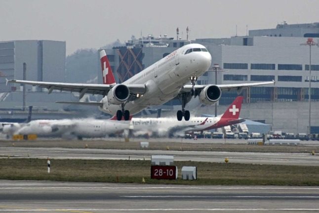 A Swiss airlines plane takes off while another can be seen on the tarmac in Switzerland