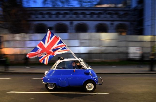 A man waves a Union Jack from the window of a European-made car.