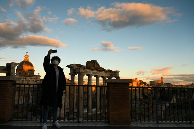 A masked tourist takes a selfie at sunset in front of Rome's Ancient Forum.