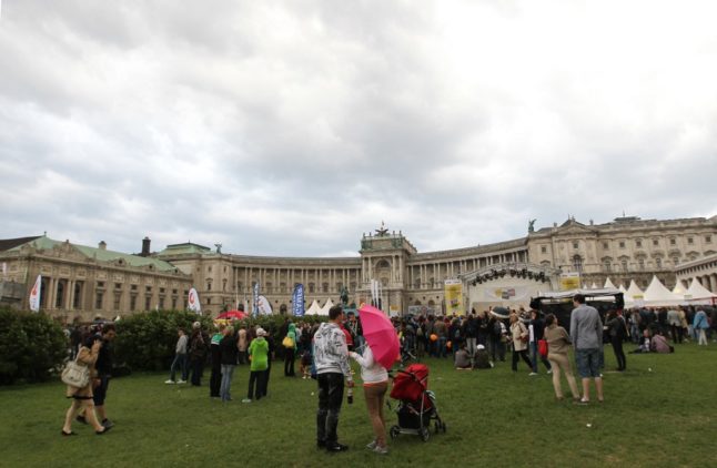 A woman protects herself from the rain (C) as people walk around Hofburg Palace in Vienna.