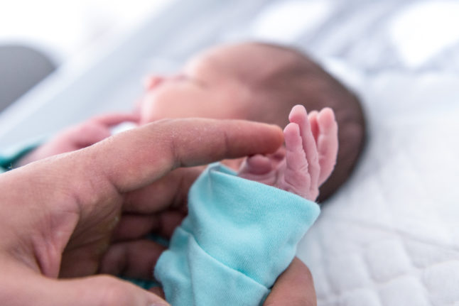 A father holds the hand of a baby boy. Babies get into bureaucracy quickly in Germany.