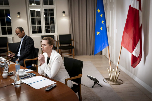 Prime Minister Mette Frederiksen sits in front of the Danish and EU flags.