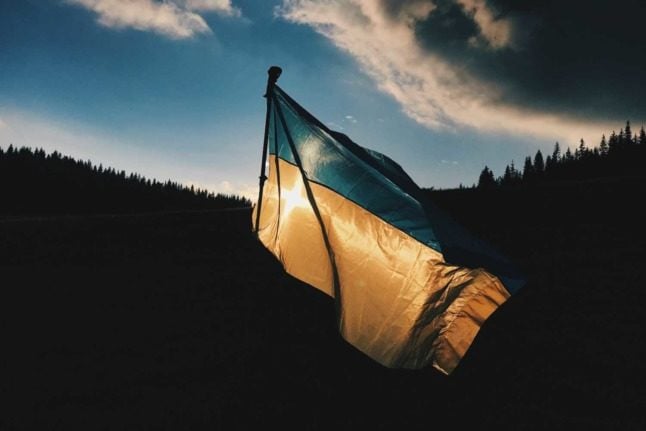A Ukrainian flag against a dark background. Photo by Max Kukurudziak on Unsplash