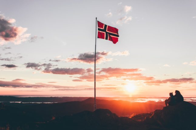 The Norwegian flag atop a mountain at sunset.
