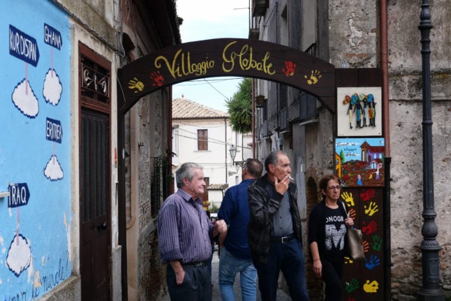 Residents of Riace walk under an arch with 'Global Village' painted on it on June 4, 2019. 