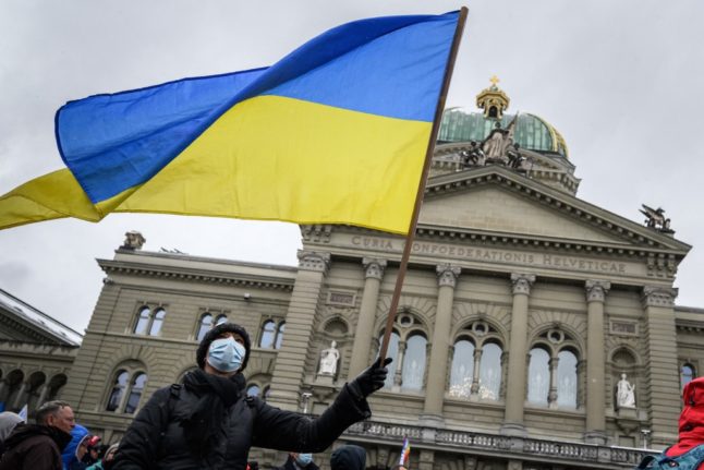 A man waves a Ukrainian flag in front of the Swiss House of Parliament