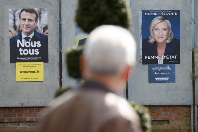A man walks by campaign posters of French presidential candidates Emmanuel Macron and French far-right party Rassemblement National (RN) Marine Le Pen