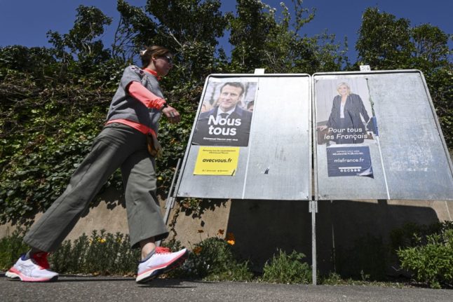 A pedestrian walks past campaign posters of French President and La Republique en Marche (LREM) party candidate for re-election Emmanuel Macron (L) and French far-right party Rassemblement National (RN) presidential candidate Marine Le Pen