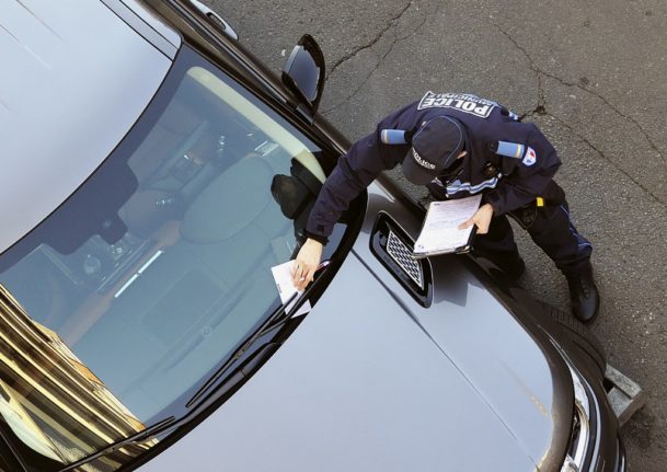 A uniformed French police officer issues a parking ticket on a car in Lille