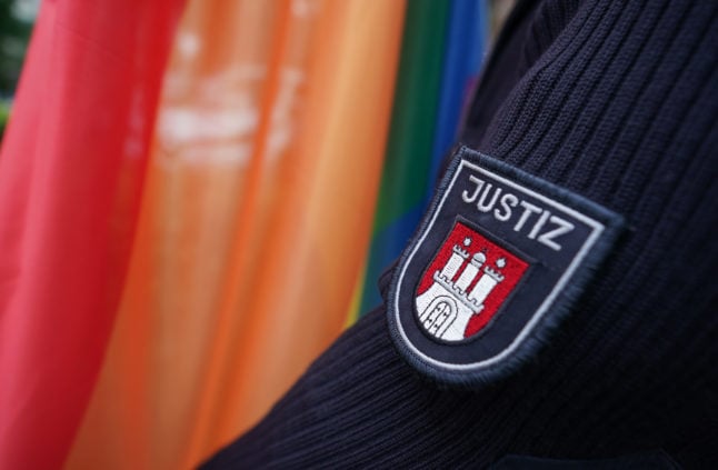 The justice emblem on the sleeve of a correctional officer is seen in front of a rainbow flag.