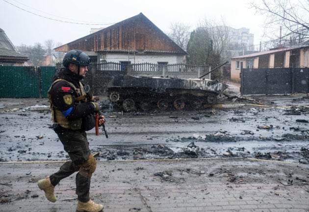 A Ukrainian soldier passes a burnt-out tank in the district of Bucha