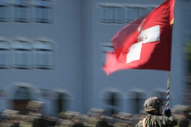 A Swiss military member holds a flag at an army exercise. Photo: Fabrice COFFRINI / AFP