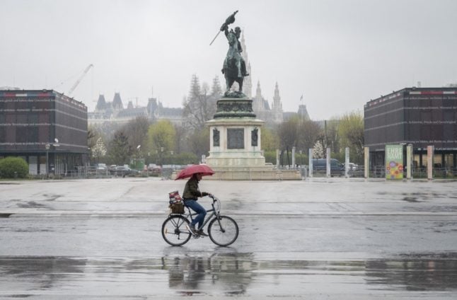 A man rides his bicycle through the deserted Helden square on a rainy day in Vienna,