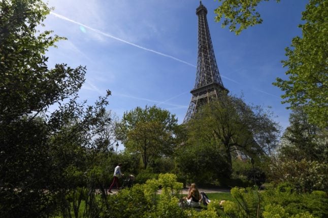 People sit below the Eiffel Tower on the Champ-de-Mars on a sunny day in Paris.