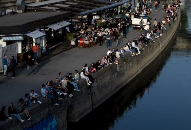 People sit in the sun at the Danube canal in Vienna, Austria .