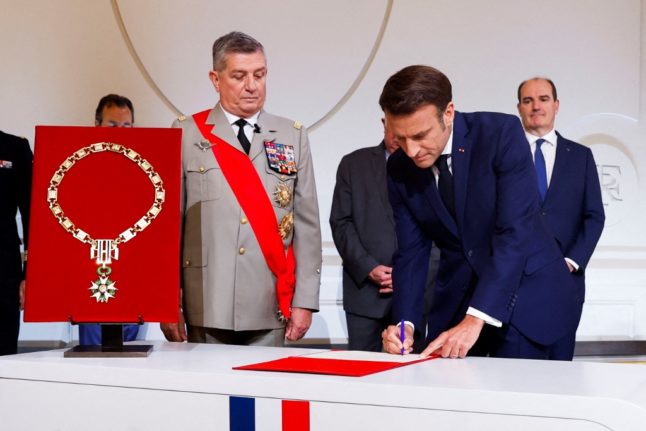 French President Emmanuel Macron (R) signs the protocol next to its great chancellor General Benoit Puga (L) at the Elysee presidential palace