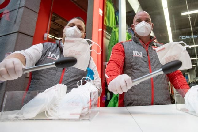 Employees of a supermarket use tongs to distribute FFP2 protective face masks to customers in Vienna.