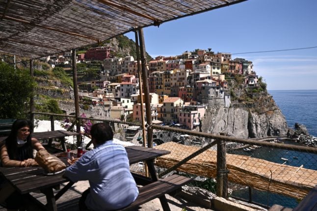 People sit at a cafe terrace overlooking the sea on June 24, 2021 in Manarola, Cinque Terre National Park, near La Spezia, Northwestern Italy.