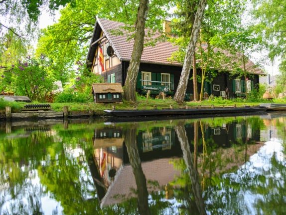 A house in the Spreewald is reflected in the water of a stream.