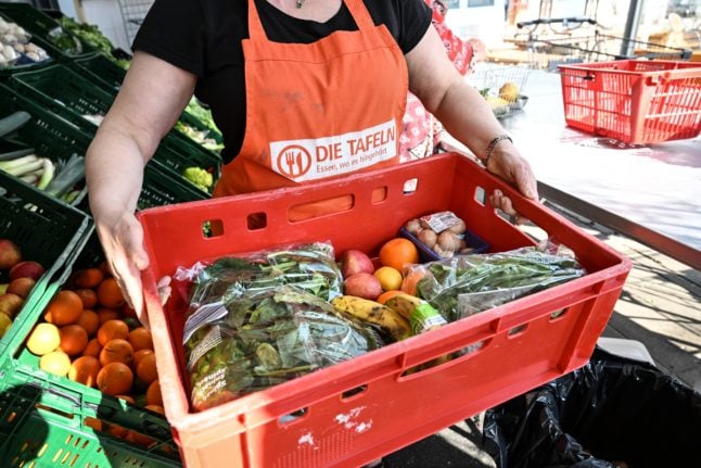 An employee at a food bank, known as the Tafel in Germany, carries a box full of fruit and vegetables.