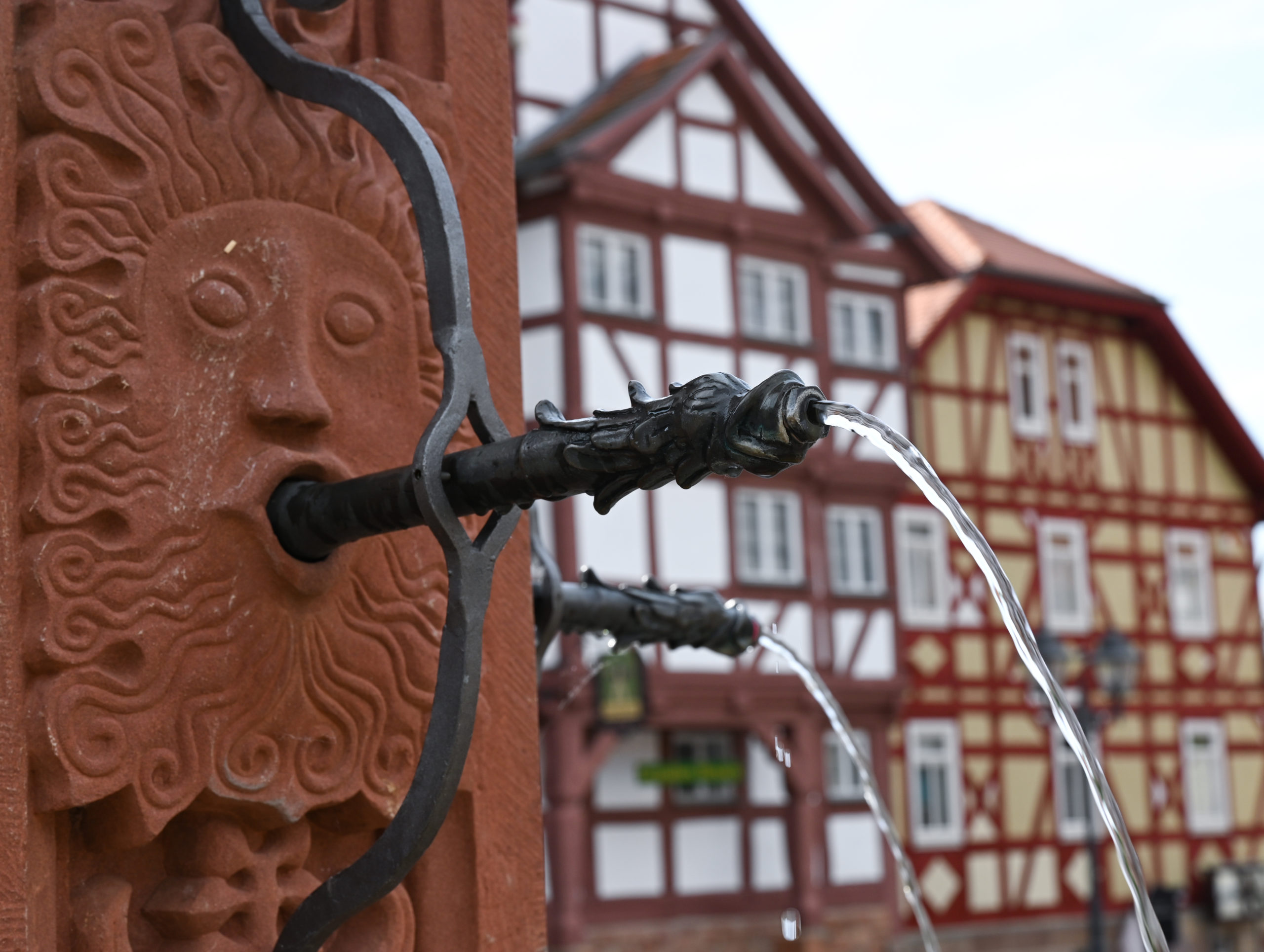 Historische Häuser mit Halbzeitungen und ein alter Brunnen auf dem Marktplatz von Hessenpark, einem beliebten Ausflugsziel in der Region Taunus. 