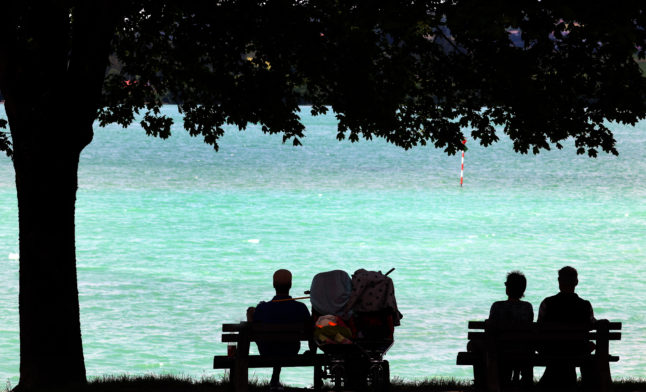 Day trippers enjoy the view of the turquoise water on the shore of Lake Forggensee in Füssen, Bavaria.