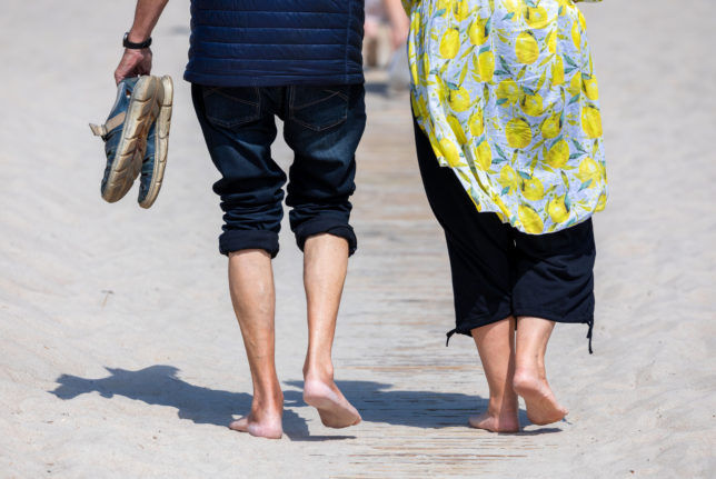 People walk barefoot on the beach in Warnemünde on the Baltic Sea coast.