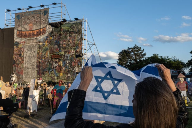 A woman stands with the Israeli flag next to a mural at the Documenta 15 exhibition on June 20th 2022.