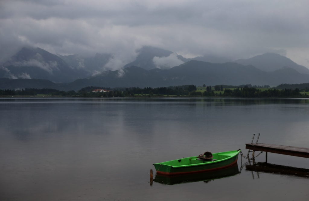 A rowing boat lies on the rainy Hopfensee lake near Hopferau (Bavaria) in front of the cloud-covered Alps in August 2016. 