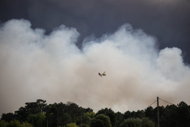 A plane flies near the smoke from a forest fire in Cazaux, France