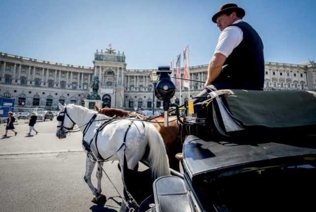 A coachman of horse driven carriages (Fiakers) passes by Hofburg palace in Vienna on a hot day. (