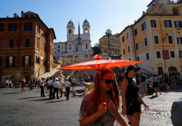 A tourist protects herself from the sun with a paper umbrella as she walks at Piazza di Spagna near the Spanish Steps in Rome. 