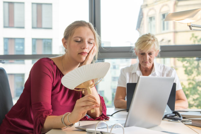 An employee fans themselves in the office on a hot day.