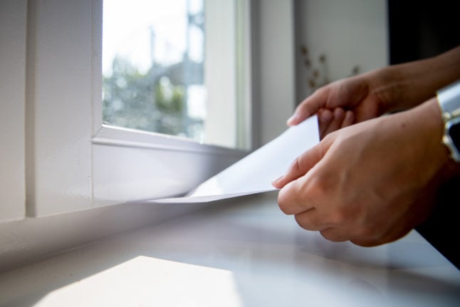 A man checks the window sealing with a sheet of paper.