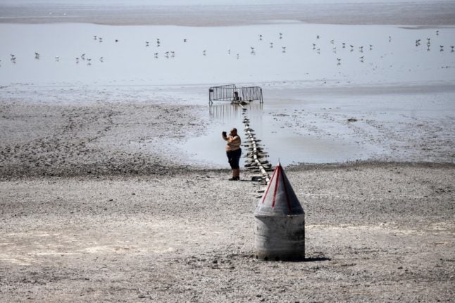 A man takes a picture standing on the dried out lake bottom of the Zicksee in St. Andrae am Zicksee in Burgenland, Austria on July 20, 2022. - Ongoing heat led to draining of the lake. Hundreds of fish died in the dried out lake. (Photo by Alex HALADA / AFP)