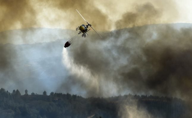 A firefighting helicopter drops water over a wildfire in spain