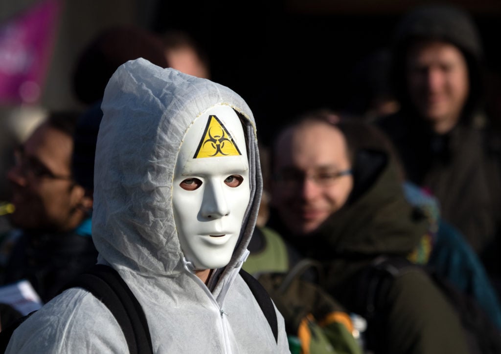 A demonstrator wears a white mask with a sticker with the symbol "biohazardous" in Berlin.