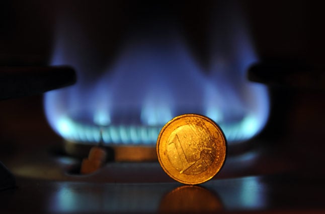 A one-euro coin stands upright in front of a flame on a gas cooker.
