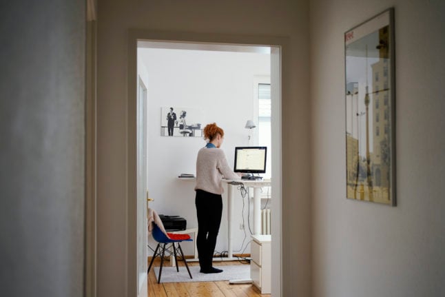 A woman uses her kitchen worktop as a standing desk while working from home.