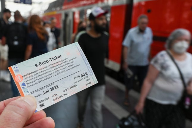 A person holds the €9 ticket in front of a regional train in Frankfurt.